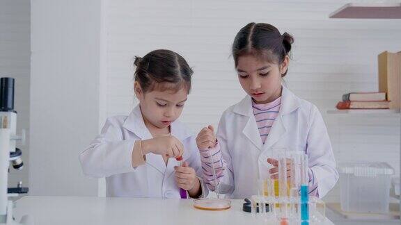 4K两个女学生穿着白色胶粘衬衫在科学教室里两人一起做化学实验在烧杯里挤水加干冰实验时兴奋的表情