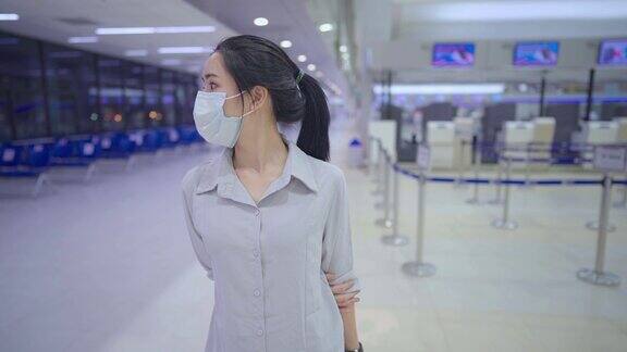 亚洲年轻女性戴着防护口罩独自行走以空空如也的机场值机柜台为背景新冠肺炎大流行新常态生活方式传染病感染