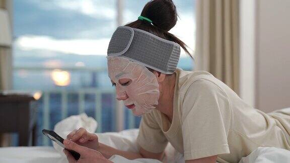 4K亚洲女人躺在床上一边用手机一边敷护肤面膜