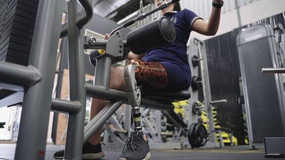 年轻女子与膝盖以上的假腿锻炼在健身房的重量训练