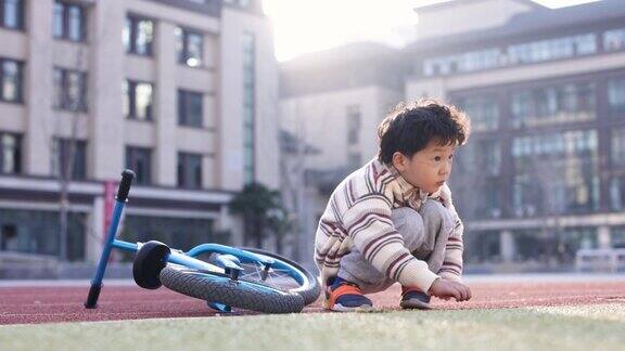 这个小男孩正在学校操场上骑自行车