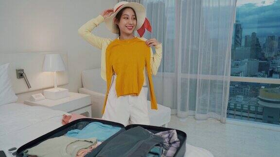 一名亚洲女性打开行李在卧室里用玻璃试衣服