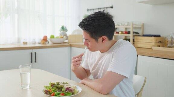 亚洲帅哥在家里厨房的桌子上吃蔬菜沙拉年轻英俊的素食男性感到快乐享受早餐与蔬菜健康的食物在家里减肥健康
