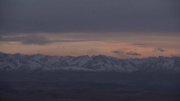 雄伟的岩石山脉在日落时覆盖着粉红色的雪随着云的流逝