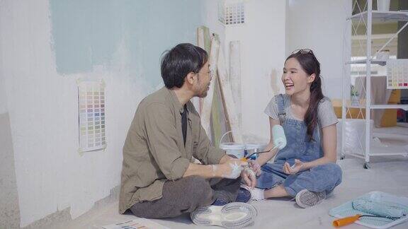 一对亚洲夫妇在粉刷房子的墙壁休息时正在聊天
