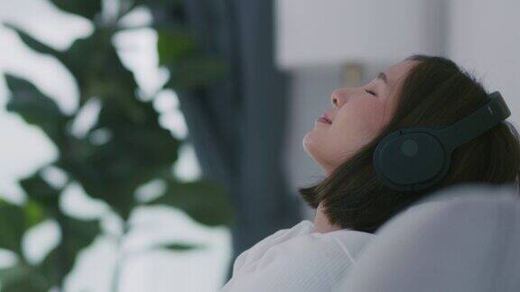快乐美丽的年轻女子戴着耳机在客厅听音乐在假日