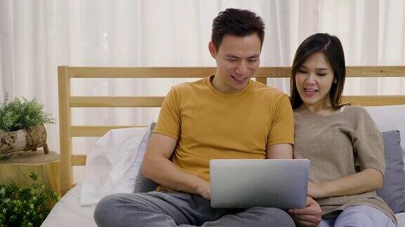 年轻的亚洲幸福夫妇使用笔记本电脑在卧室夫妇放松和花时间在一起在家里