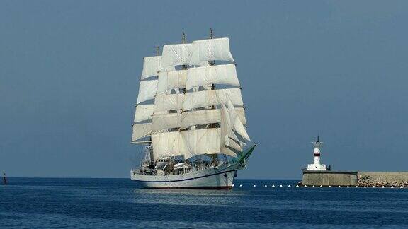 一艘美丽的老式帆船在灯塔的背景下驶入港口