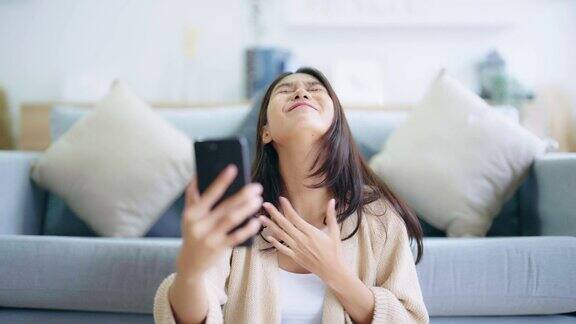 快乐的年轻亚洲女子放松在舒适的沙发上在家里发短信在手机上微笑的女孩使用手机网上聊天信息网上购物从家里