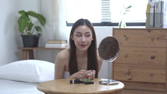 美丽的年轻亚洲女人在家里的卧室里化妆