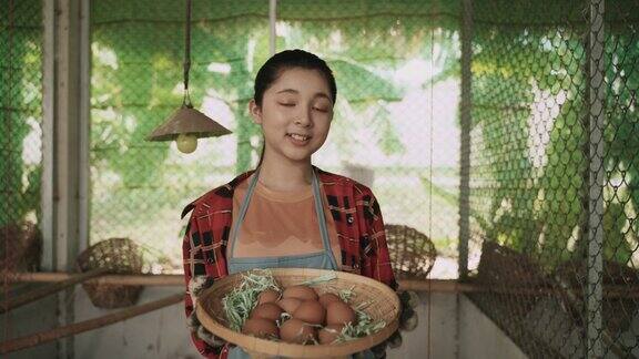 肖像快乐的亚洲少女农民站在鸡蛋篮子和看着相机在鸡舍在有机农场