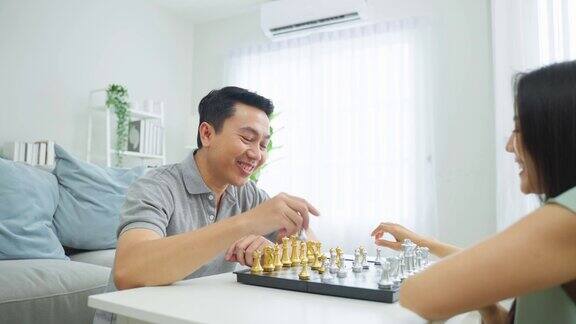 亚洲有吸引力的夫妇在家里的客厅下棋幸福的家庭年轻的男人和女人感到快乐和放松一起度过自由的闲暇时间关系生活方式