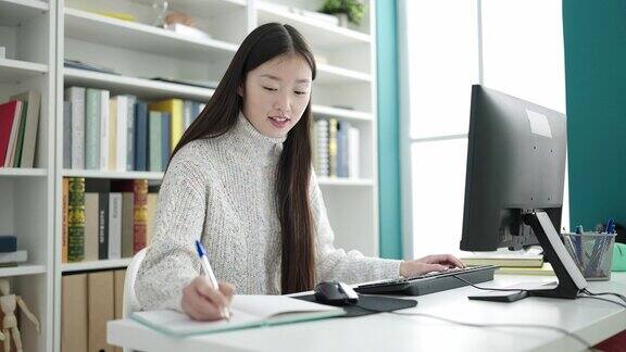 年轻的中国女学生在图书馆大学用电脑在笔记本上写字