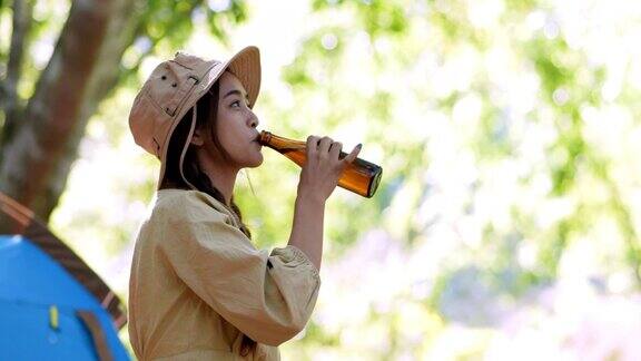 年轻女子戴着帽子在露营帐篷前喝饮料