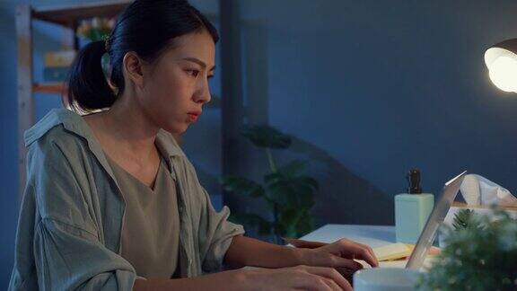 年轻的亚洲自由职业女性使用笔记本电脑在家里的客厅晚上