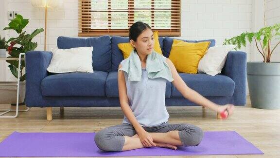 年轻的亚洲女子在自家客厅的垫子上练习哑铃人们健康的生活方式幸福的生活