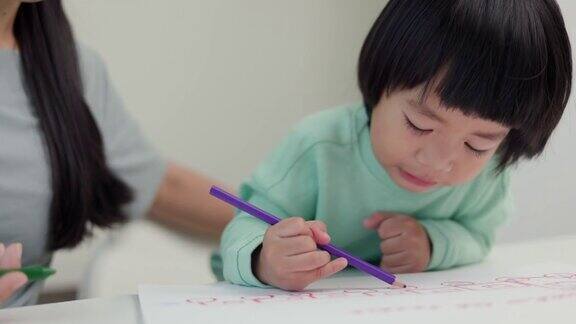 妈妈教儿子如何用蜡笔在书上画画或做作业快乐的亚洲男孩与他的母亲在客厅里用蜡笔和彩色铅笔画画家庭