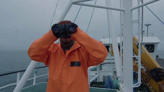 穿着防护服的商业渔船船长透过望远镜看