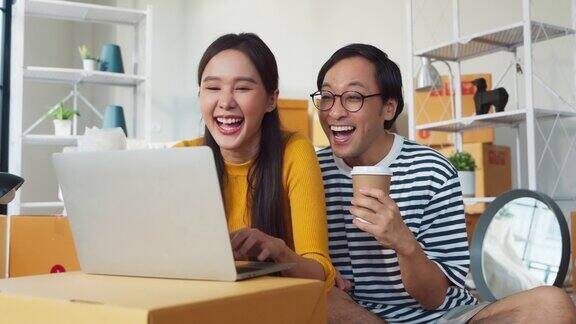 微笑着享受家搬家休息幸福亚洲人结婚夫妇坐在地板上用笔记本电脑搜索卡车运送新家搬迁家搬家的想法概念亚洲人打包箱子搬家