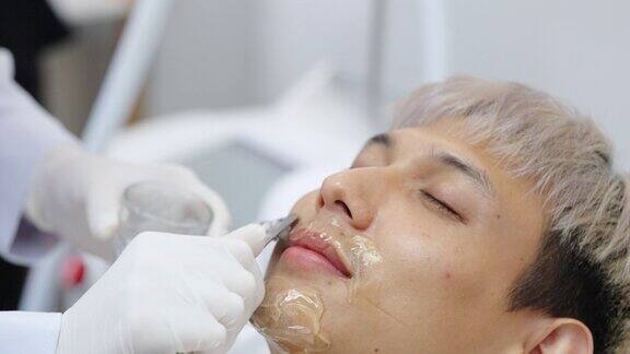 4K美容师在美容诊所进行激光脱毛前在亚洲男性脸上涂抹冷却凝胶