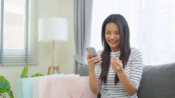 亚洲美女喜欢在家里的客厅网上购物漂亮的女孩坐在沙发上用手机在网上商店购买商品后拿着信用卡进行网银网上支付