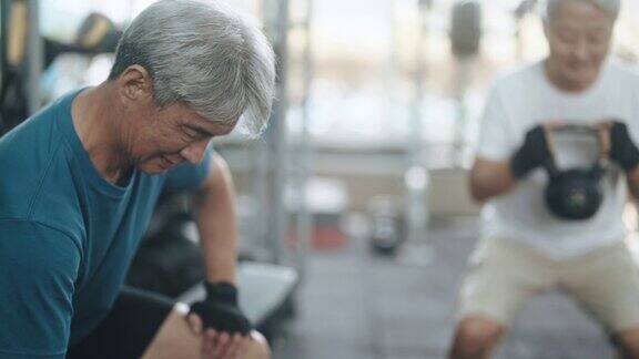 2名活跃的中国老年男子在健身房进行壶铃和哑铃力量训练