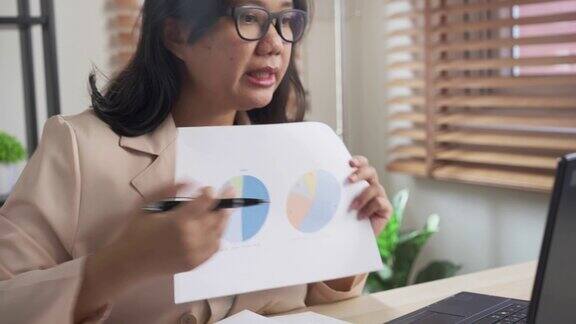 亚洲妇女与商业规划图纸会议在视频会议上的笔记本电脑在家里工作