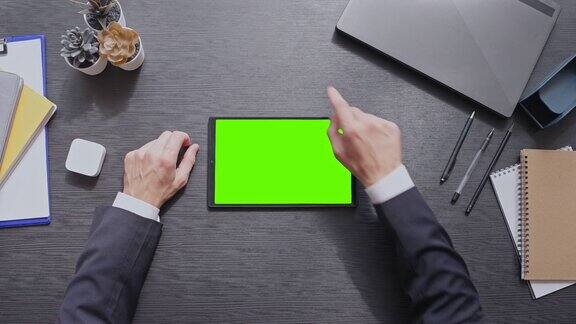 一名男子坐在办公室里用绿色屏幕在平板电脑上滚动网页