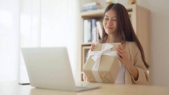 年轻的亚洲妇女在家里使用笔记本电脑女性在和朋友视频聊天时展示礼盒生日快乐新年快乐感恩节快乐