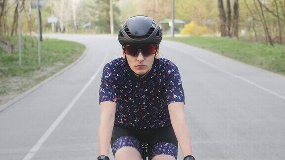 专注于女自行车手在公园里骑自行车前视图戴着黑色头盔和眼镜