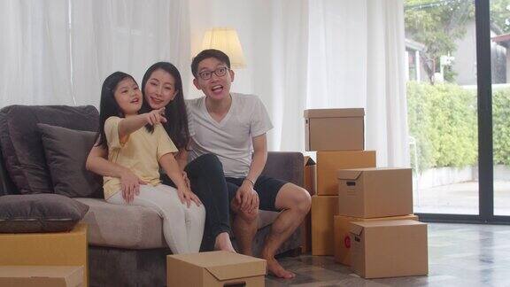 快乐的亚洲年轻家庭业主买了新房日本的妈妈爸爸和女儿拥抱期待未来在搬家后的新家与盒子一起坐在沙发上