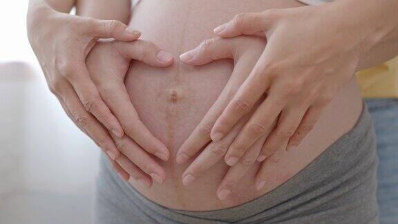 亚洲孕妇和丈夫在家里做心形手势拥抱在肚子上怀孕产妇准备和预期