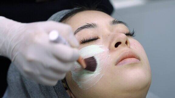 4K美容师在亚洲女性脸上涂抹护理面膜