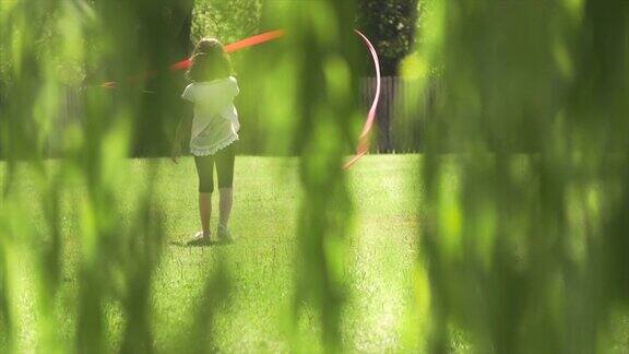 小女孩在夏令营玩粉红丝带带在绿色草地上做体操慢动作