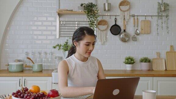 年轻的亚洲女商人在家里的厨房里使用电脑笔记本电脑工作在家工作
