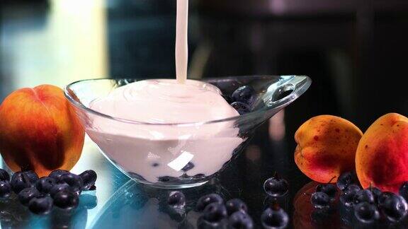 把蓝莓和浓稠的酸奶油倒在玻璃盘里旁边是桃子和杏蓝莓酸奶美味的液体白酸奶油和蓝莓的质地奶油乳制品