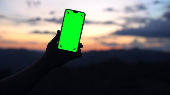 男人拿着智能手机的绿色屏幕与自然戏剧性的天空为背景色度键