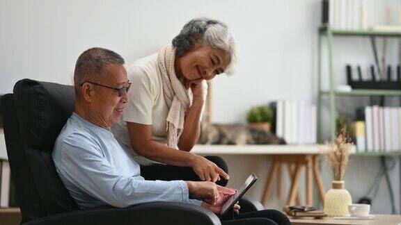 可爱的老年夫妇在舒适的家中放松时使用数码平板电脑老年人的生活方式和婚姻观念