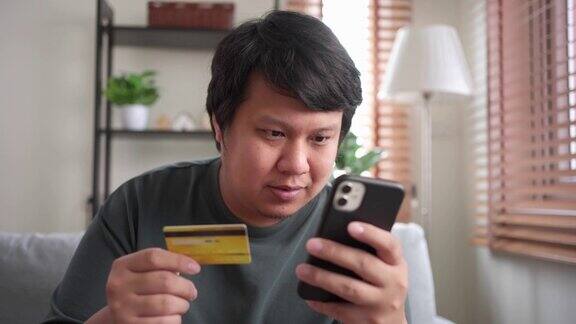 坐在客厅沙发上的男人用智能手机刷卡购物的特写