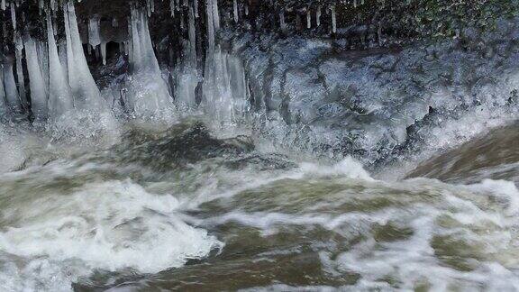 在寒冷的冬天流动的河流和冰柱