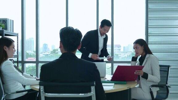一群年轻的亚洲企业家高层管理人员正在一间有自然光窗户的会议室里开会审查来自团队的股票投资数据