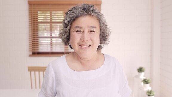亚洲老年妇女感到幸福的微笑和看着镜头而放松在客厅的沙发在家里生活方式高级女性在家
