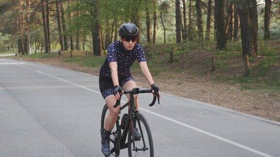 女孩骑着黑色的自行车穿着蓝色的运动衫和黑色的头盔在公园里骑为自行车比赛进行训练