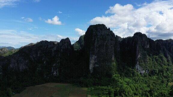 在老挝万荣(VangVieng)在雨季、季风和无人机的帮助下喀斯特山峰俯瞰着森林旁边的绿色水稻田