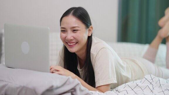 4K年轻的亚洲女子在卧室的床上用笔记本电脑工作