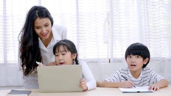 在家教育技术亚洲年轻的母亲在教家庭作业的儿子和女儿在客厅小女孩坐在看平板电脑寻找学习信息