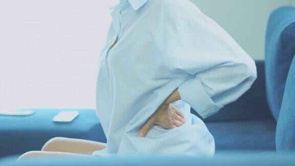 美丽的亚洲妇女遭受背痛按摩在她的背部而坐在家里的沙发保健和医疗