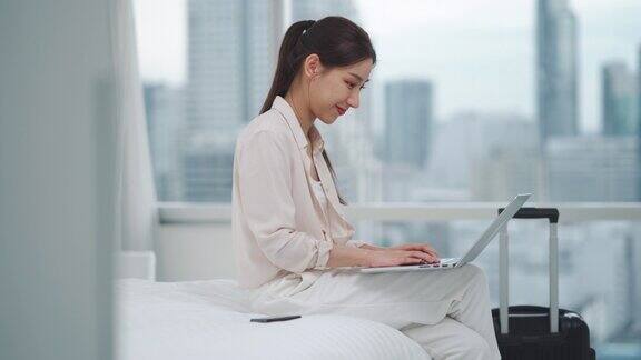 亚洲女商人在进入房间时使用科技平板电脑在床上工作