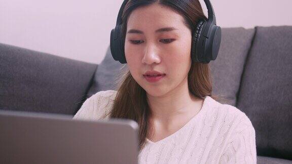 一位美丽的亚洲女性戴着耳机在家里用笔记本电脑工作