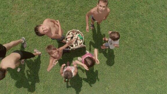 俯视图夏令营的孩子们在绿色的草地上玩耍把海绵放在箱子里慢镜头空中垂直